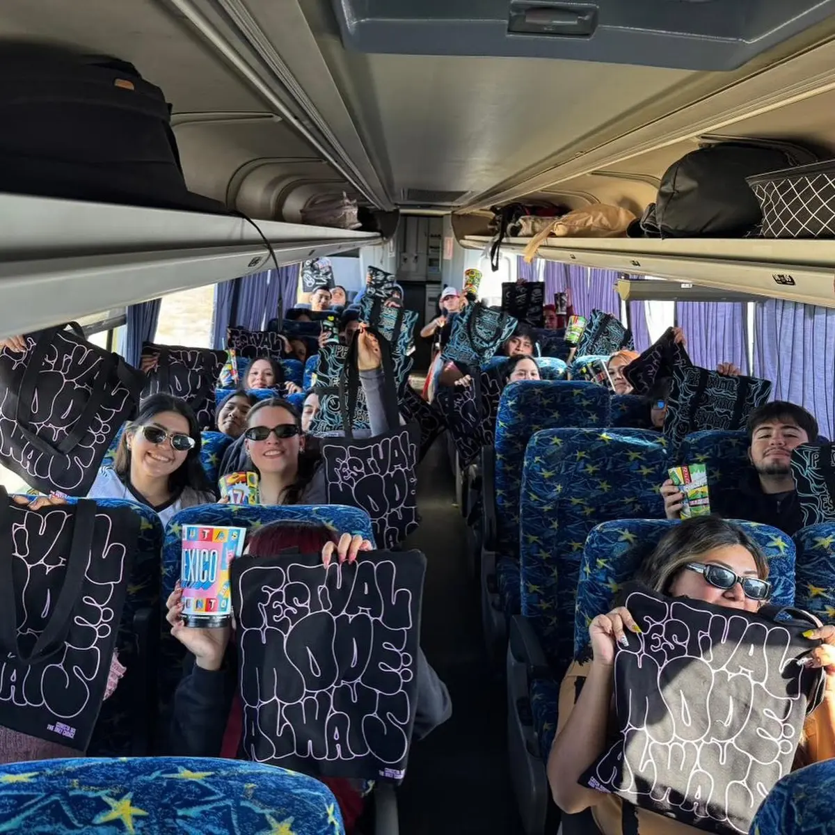 Viajeros mostrando sus tote bags del evento dentro del camión de turismo